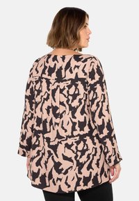Blusa a maniche lunghe in morbido tessuto rosa chiaro con un motivo astratto nero. Vestibilità ampia con scollatura a barca e dettagli di pieghe sottili.