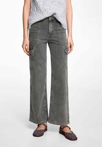 Bredvidsbyxor i grå denim med ficklock, distinkta sömmar och en lätt urtvättad struktur. Diktas med svarta och rosa skor.