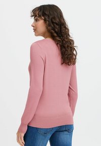 Pull rose à manches longues en maille douce, avec un col rond et des poignets côtelés, associé à un jean bleu.
