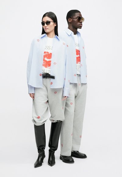 Light blue oversized shirt, white graphic tee with red lips, gray sweatpants with lip prints, black knee-high boots, and sunglasses.