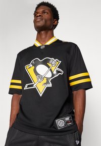 Fekete jégkorong mez sárga kiegészítőkkel és csíkokkal, elöl a Penguins logójával. Anyaga hálós, laza szabású.