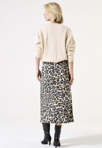 Pull beige avec épaules tombantes associé à une jupe imprimé léopard arrivant aux genoux. Des bottes noires à talons hauts complètent le look.