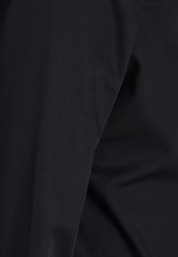 Zwarte stof in close-up, gladde textuur met subtiele glans. Heeft een op maat gemaakte vorm, zonder zichtbare patronen of hardware-details.