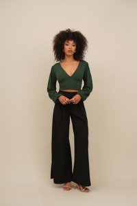 Zelený dlouhý rukáv cropped top s hlubokým V-výstřihem, v kombinaci s černými širokými kalhotami. Hladká látka a viditelné zlaté akcentové prsteny.