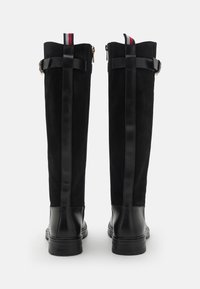 Schwarze knielange Stiefel mit Wildleder-Obermaterial und Lederakzenten, ausgestattet mit einem Reißverschluss auf der Rückseite und einem kontrastierenden gestreiften Ziehband an der Oberseite.