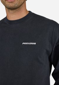 Dark gray long-sleeve t-shirt made of cotton, featuring a round neckline and white embroidered "PEGADOR" logo at the chest.