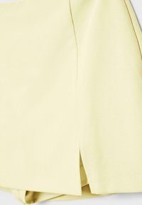 Close-up of pale yellow fabric with a central seam and a small side slit at the bottom hem.