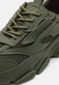 Zapatillas verdes con un diseño de malla y acentos de goma suave, cordones texturizados y una suela gruesa con una banda de rodadura con patrón.