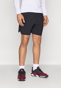 Μαύρο αθλητικό σορτς από ελαφρύ ύφασμα με άνετη, φαρδιά εφαρμογή. Φοριέται με μαύρα και κόκκινα αθλητικά παπούτσια και λευκές κάλτσες μέχρι τον αστράγαλο.