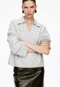 Grauer, weicher Wollpullover mit einem Schalkragen, kombiniert mit einem eleganten, glänzenden schwarzen Lederrock. Der Stoff hat eine subtile Textur.