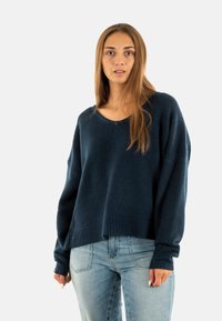 Maglione oversize di colore blu scuro, con scollatura ampia e polsini a coste. Texture leggera, abbinato a jeans azzurri.