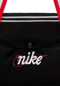 Juoda audinio maišelis su raudonomis petnešomis, baltomis užtrauktukų juostelėmis ir baltu siuvinėtu 'nike' tekstu su raudonu swoosh logotipu.