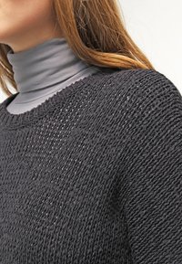 Maglione lavorato a maglia grigio scuro con una trama allentata e scollo rotondo, indossato sopra un dolcevita grigio chiaro. Tessuto strutturato e design casual.