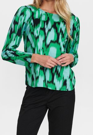 Groene en turquoise lange mouw blouse met een gedurfde abstracte patroon. Zacht materiaal en een ontspannen pasvorm, gecombineerd met donkere broeken.