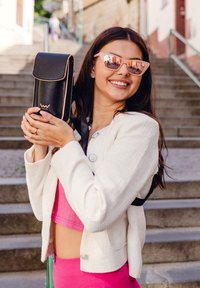 Black leather bag with rose gold accents, rectangular shape, adjustable strap, held by a person wearing a white textured jacket and pink top.