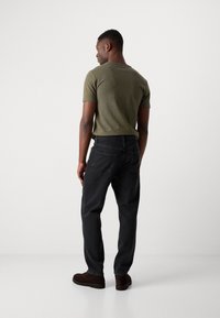 Dark gray denim pants with a relaxed fit, paired with an olive green short-sleeve shirt. The outfit includes brown footwear with a smooth texture.