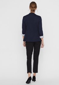 Marinblå blazer med skräddarsydd passform, trekvartsärmar och ränder vid muddarna. Svarta smala byxor och svarta högklackade skor fulländar outfiten.