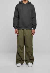 Tummanharmaa huppari, jossa on etutasku ja kiristysnauharoidat, yhdistettynä väljälahkeisiin oliivinvihreisiin housuihin. Valkoiset tennarit täydentävät asun.