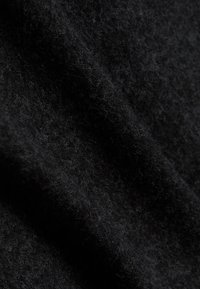 Gros plan sur un tissu en laine noire texturée avec des fibres visibles et de doux plis créant des ombres subtiles.