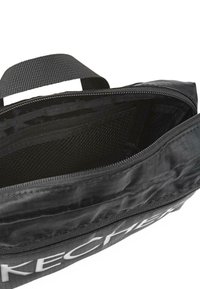 Bolsa textil negra con abertura con cremallera, que presenta una textura exterior suave y un bolsillo de malla en el interior. "SKECHERS" impreso de manera prominente.