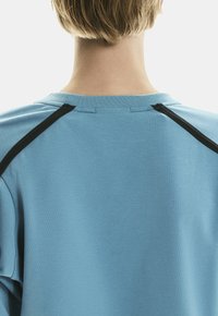 T-shirt bleu clair avec un col rond et des accents noirs au niveau des épaules. Tissu doux et lisse avec une coupe décontractée.