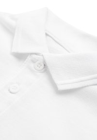 Col polo en tissu blanc texturé avec deux boutons blancs sur la patte de boutonnage, montrant en gros plan les détails du tissu et les coutures.