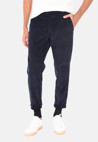Pantaloni in corduroy blu navy con superficie texturizzata, taglio affusolato e tasche anteriori, abbinati a sneakers bianche e calze nere.