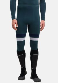 Eng anliegende thermische Leggings in tiefem Teal mit weißen und marineblauen Streifen. Kombiniert mit hohen Socken, die graue und schwarze Akzente aufweisen.