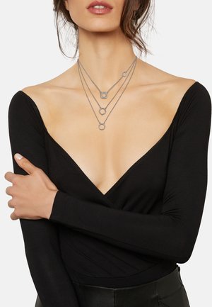 Zilveren dr laagse ketting met cirkelvormige en vierkante bedels. De kettingen zijn delicaat, in combinatie met een diep V-hals zwart top.
