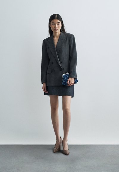 Gray pinstripe double-breasted blazer over a dark denim mini skirt, paired with beige high heels. Holds a blue patterned clutch.