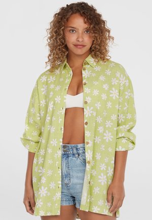Groen overhemd met knopen, bedekt met een wit madeliefjesmotief, lange mouwen, comfortabele pasvorm, gestructureerde stof, gecombineerd met denim shorts.