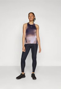 Canotta racerback in tonalità di viola con design sfumato, abbinata a leggings neri e scarpe da ginnastica nere. Tessuto liscio e aderente.
