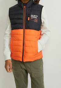 Kamizelka puchowa w czarno-pomarańczowym kolorze z zamkiem błyskawicznym z przodu, wysokim kołnierzem i pikowanym wzorem. Posiada kieszeń na piersi z logo.