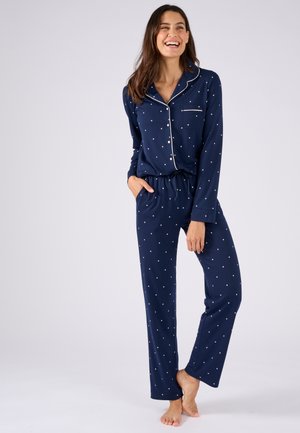 Marineblauw pyjama set met witte stippen, lange mouwen, knoopsluiting aan de bovenkant en broek met elastische taille. Zachte stof met contrasterende pipingdetails.