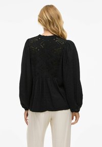 Blusa nera con maniche a sbuffo, parte anteriore texturizzata e retro ricamato con dettagli geometrici e accentuazioni a taglio.