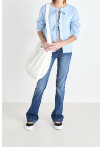 Cardigan côtelé bleu clair avec un nœud central, associé à un jean évasé. Sac à épaule blanc texturé avec des accents ronds. Chaussures noir et blanc.