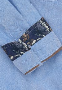 Lichtblauw linnen overhemd met kraag, met een donker bloempatroon voering en bruine accenten, voorzien van zichtbare stikseldetails.