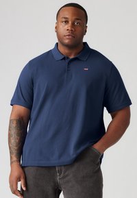 Marineblauwe polo met een klassieke kraag, korte mouwen en een klein rood Levi's-logo op de borst. Zacht katoen, comfortabele pasvorm.