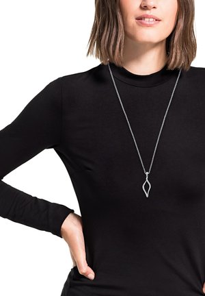 Zilveren hanger met een bladvormig ontwerp, hangend aan een fijne ketting, gedragen boven een hoge hals zwarte lange mouwen shirt.