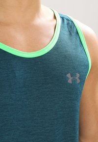 Blågrön linne med en slät textur, med neongrön kanting och en grå logotyp på bröstet.