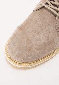 Beige suede shoe with a rounded toe, featuring light stitching and a rubber sole with a contrasting beige edge.