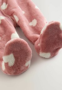 Rosa, flauschige Overallbeine mit weißen Herzmustern. Weicher Stoff und abgerundete Fußöffnungen für optimalen Komfort.