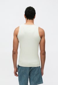 Light gray, fitted tank top made of ribbed fabric, with a crew neckline and no visible logos or patterns, paired with blue textured shorts.