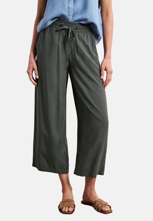 Luźne ciemnozielone krótkie spodnie z sznurkiem w pasie, noszone z jasnoniebieską koszulką bez rękawów i brązowymi sandałami wsuwanymi.