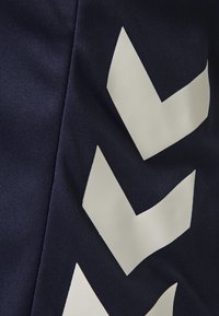 Zbliżenie ciemnej tkaniny z trzema dużymi białymi wzorami w kształcie jodełki ułożonymi pionowo.