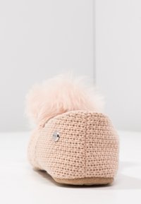 Svetle růžové pletené bačkory s texturovaným tělem, chlupatou bambulí na zadní straně a malým kovovým logem. Měkká podešev.