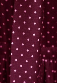 Bordowa tkanina w małe różowe kropki, charakteryzująca się miękką teksturą i lekko drapowanym fasonem. Zauważalna dzięki swojemu zabawnemu wzorowi.
