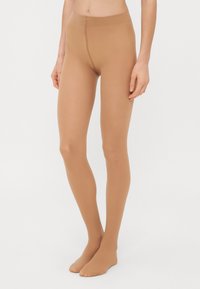 Collants opaques beiges avec une texture lisse, un design sans couture et une taille haute, offrant une couverture complète des jambes sans coutures visibles.