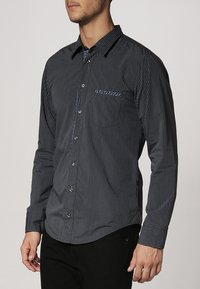 Zwart en marineblauw gestreept overhemd met knopen, een kraag, lange mouwen en een borstzak. Gemaakt van een lichtgewicht stof met een gladde textuur.