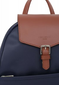 Zaino in tessuto blu mare con pattina in pelle marrone e accessori in argento. Presenta una chiusura cucita e il logo "HEXAGONA PARIS" sulla pattina.